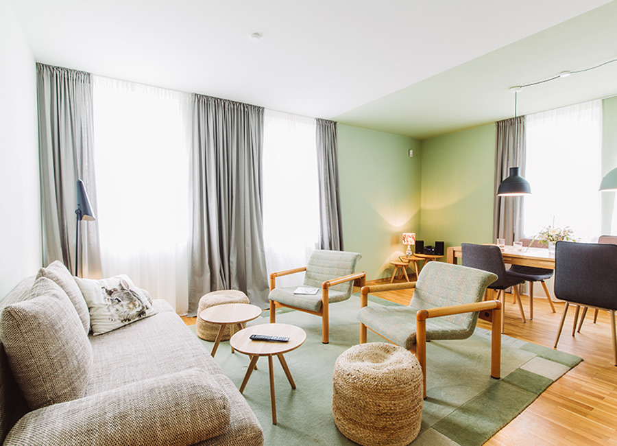 Helles Wohnzimmer mit Sofa, Sesseln und grünem Teppich